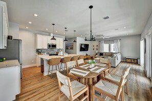 A modern kitchen with white cabinets, a dining area with wooden chairs, and a living room with a sofa and TV. - Pool Home Pet Friendly  Fenced Yard  Near Beach (Fort Myers)