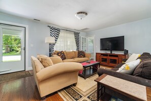 Ein Wohnzimmer mit einem beigen Sofa, einem braunen Sofa, einem Couchtisch, einem Fernseher und einem gemusterten Teppich.
