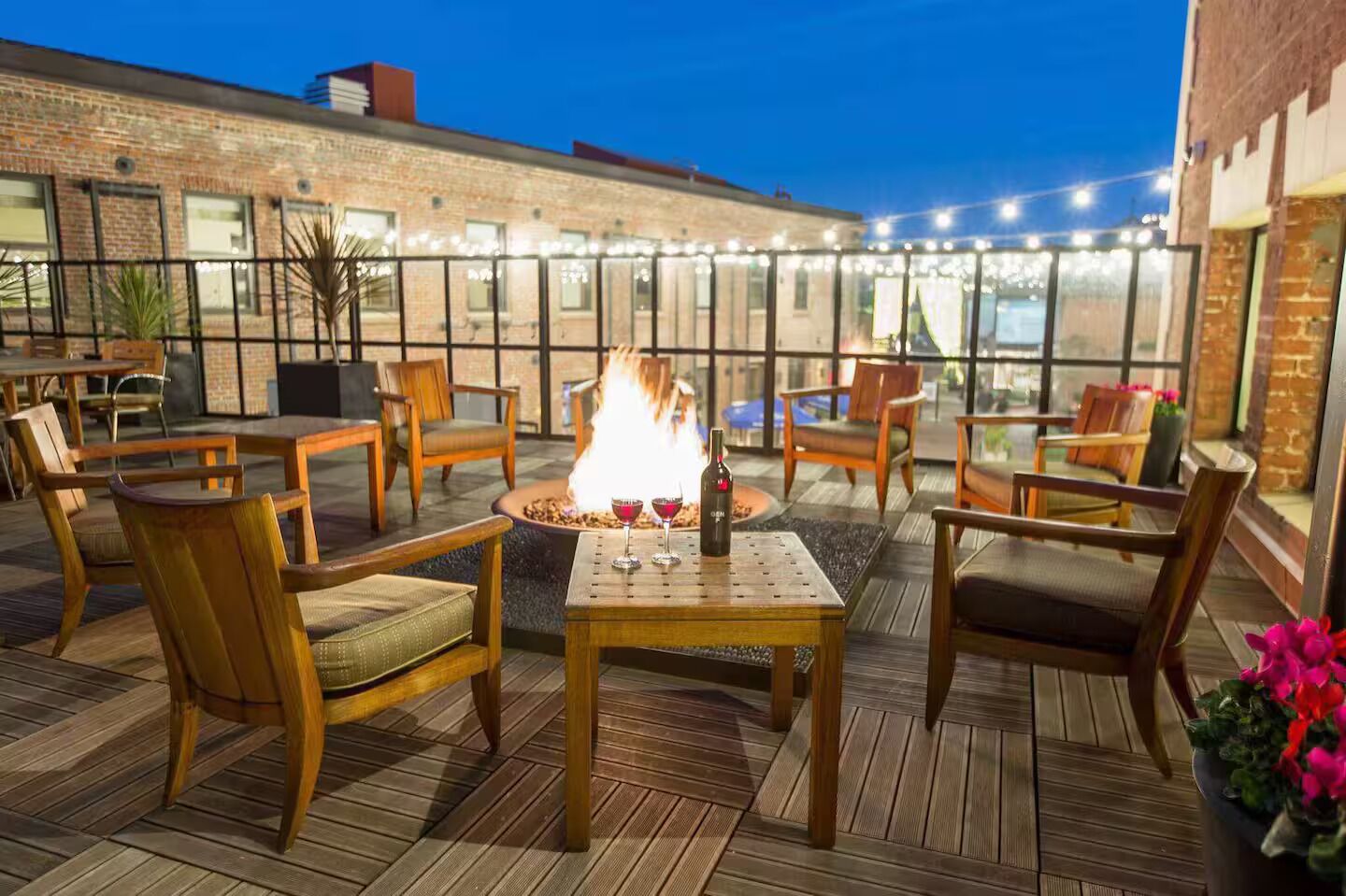 An outdoor patio with wooden furniture, a fire feature, and string lights.