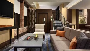 Ein modernes Wohnzimmer mit Sofa, Couchtisch, an der Wand befestigtem Fernseher, Treppe und einer dekorativen Wandverkleidung.