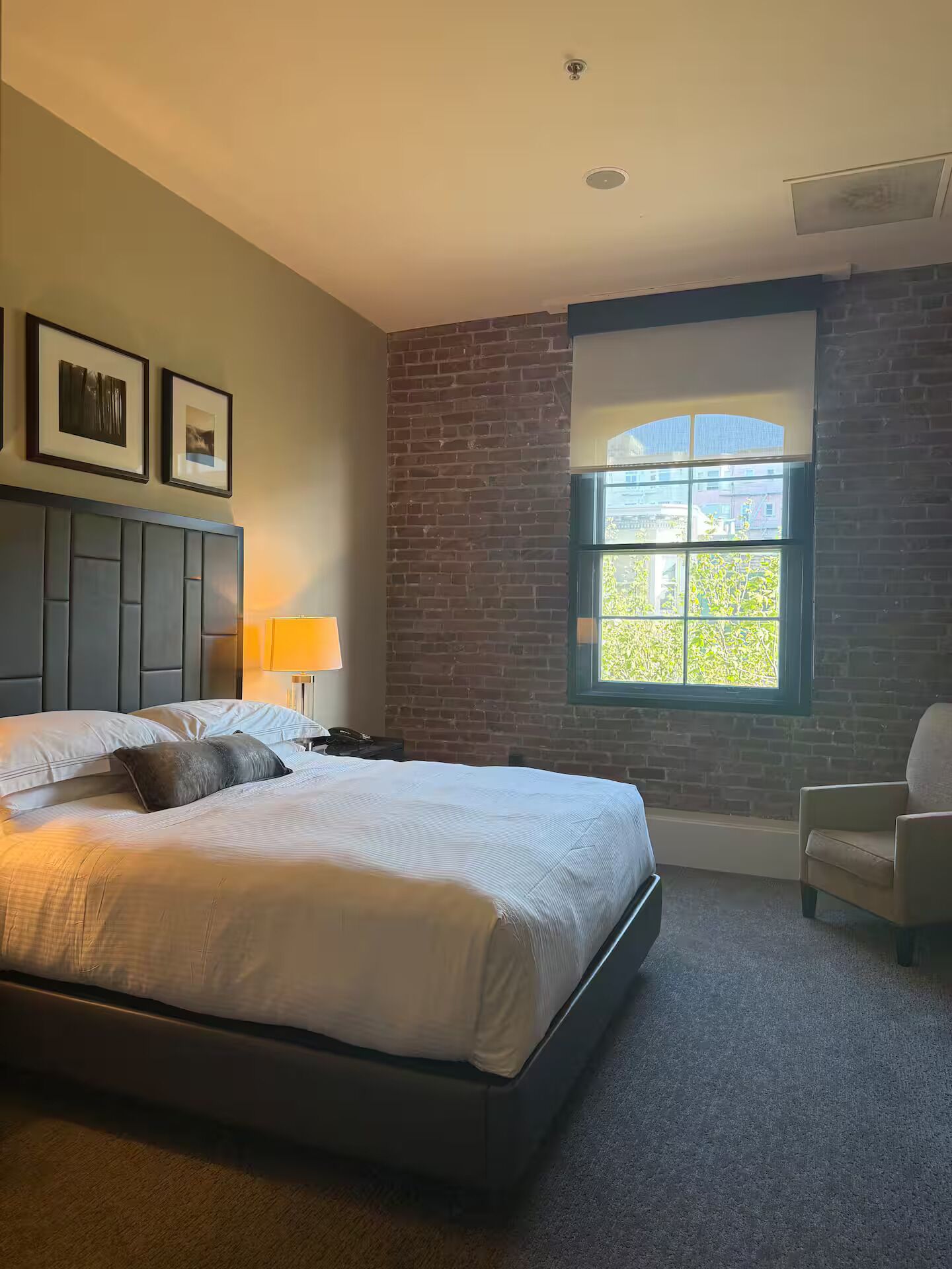 Une chambre à coucher avec un lit, une table de chevet, une chaise, une fenêtre et un mur en briques.