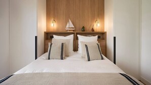 Un dormitorio con cabecera de madera, dos mesitas de noche, una cama con ropa de cama blanca y dos lámparas fijadas a la pared.