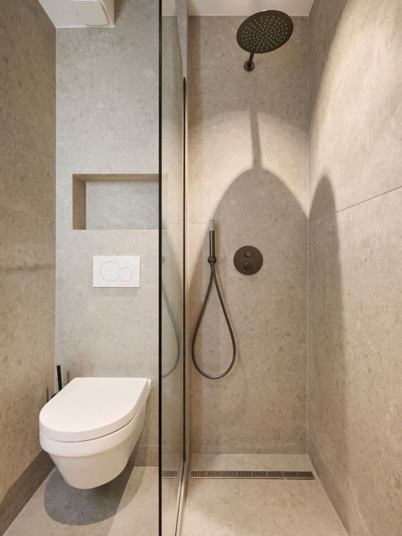 Een moderne badkamer met een glazen douchewand, toilet, douche met handdouche en een bedieningspaneel aan de muur.