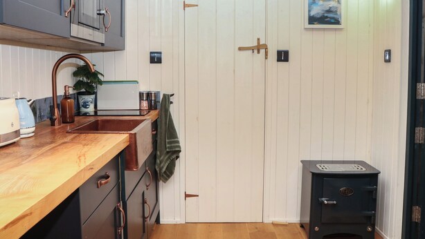 Una cocina con encimera de madera, grifos de cobre, estufa y puerta blanca.