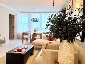 A modern living room with a sofa, coffee table, and a large vase of greenery. - Two King Beds | Ocean Views | Beachfront Steps (San Juan)