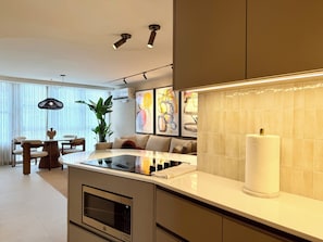 A modern kitchen with a central island, a dining area with a table and chairs, and a living space with a sofa and a large plant. - Two King Beds | Ocean Views | Beachfront Steps (San Juan)