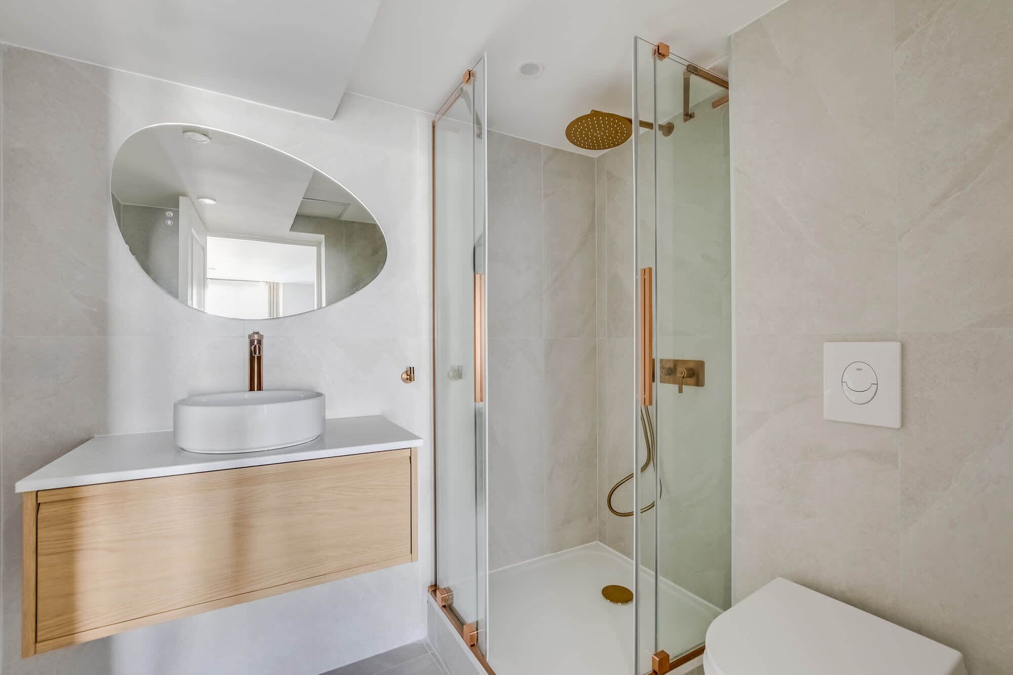 A modern bathroom with a round mirror, a white sink, a glass-enclosed shower, and a toilet.