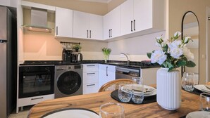 Een moderne keuken met witte kasten, een ingebouwde oven, een wasmachine en een eethoek met een houten tafel en stoelen.