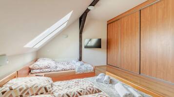 A bedroom with a sloped ceiling, a bed with patterned bedding, a wooden wardrobe, and a television mounted on the wall.