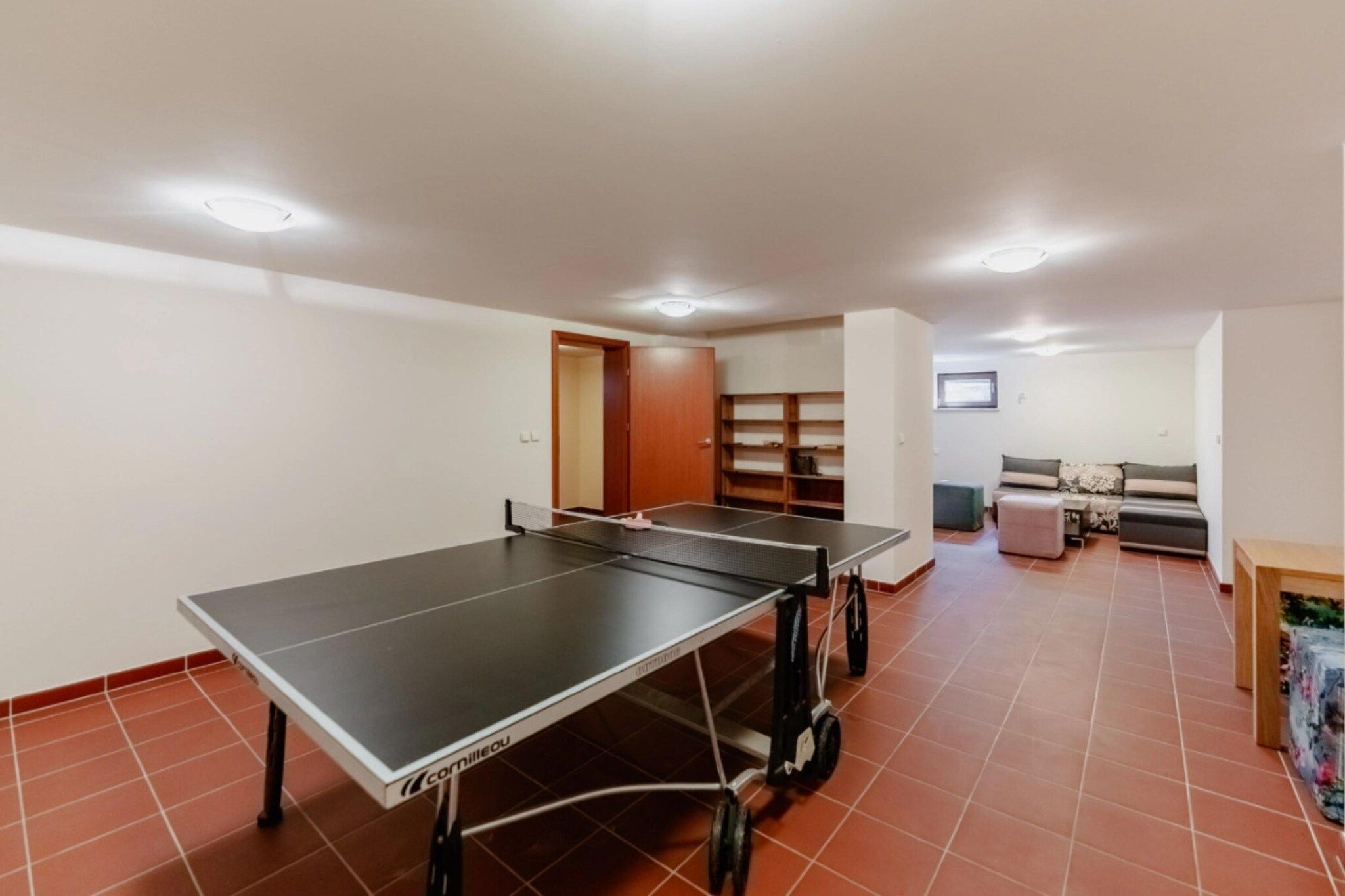 A room with two ping pong tables, a sofa, and a small table with a TV.