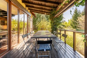 An outdoor deck with a table and chairs, surrounded by glass doors and a wooden railing. - Large, comfortable holiday home with a garden (Zatom)