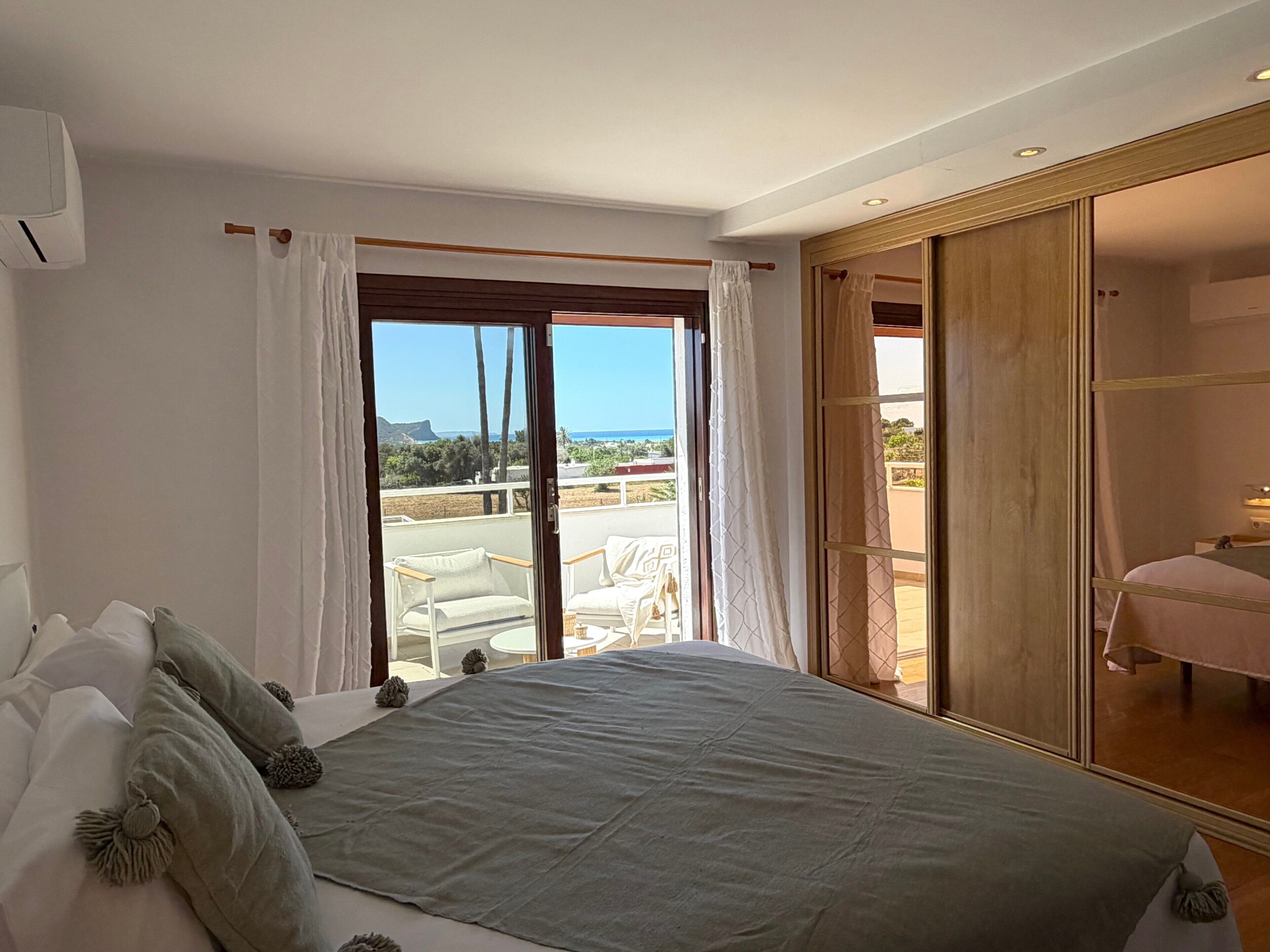 Ein Schlafzimmer mit Bett, Blick auf einen Balkon und einer Schiebetür zum Badezimmer.