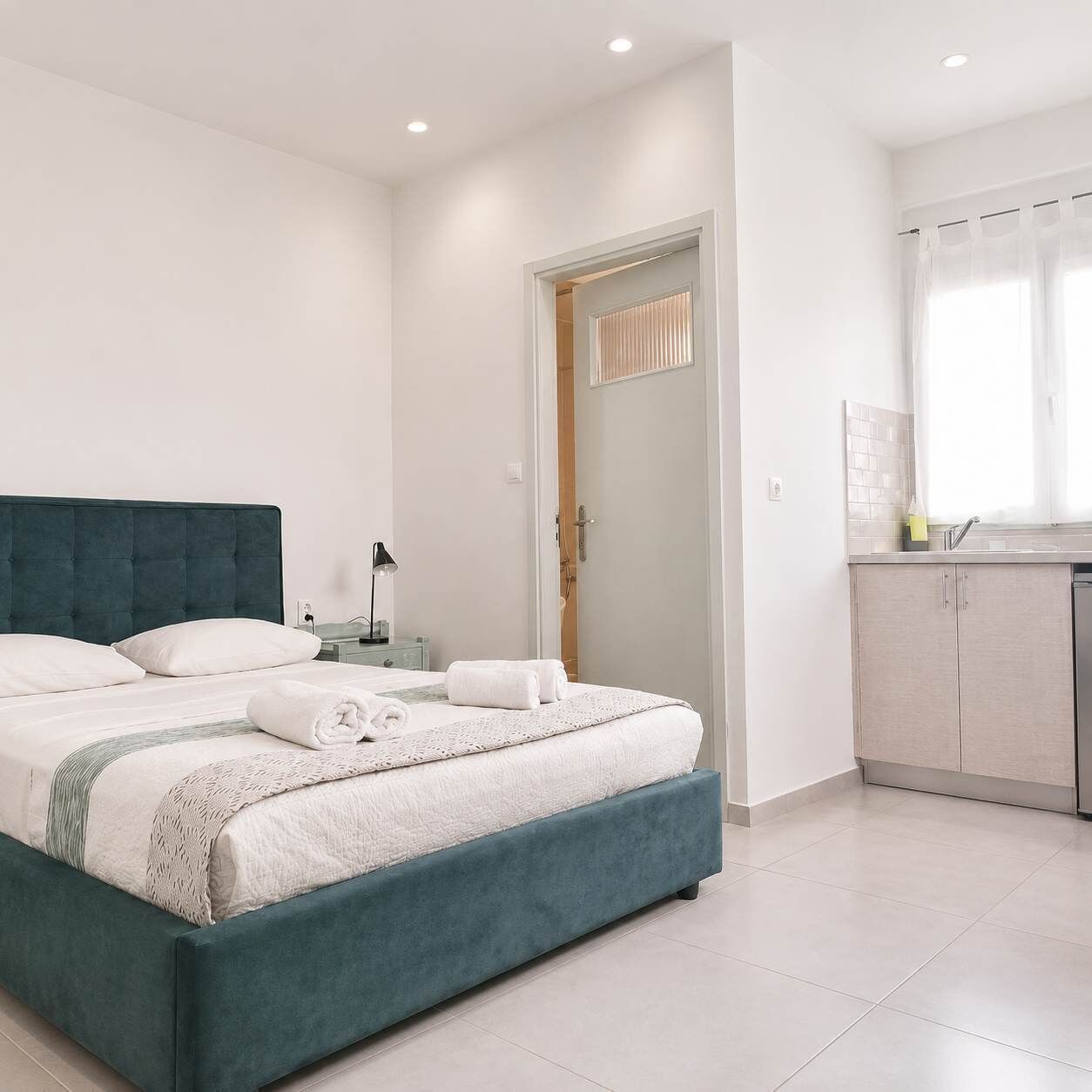 Un dormitorio moderno con una cama grande, una mesita de noche con lámpara y un baño visible a través de una puerta abierta.