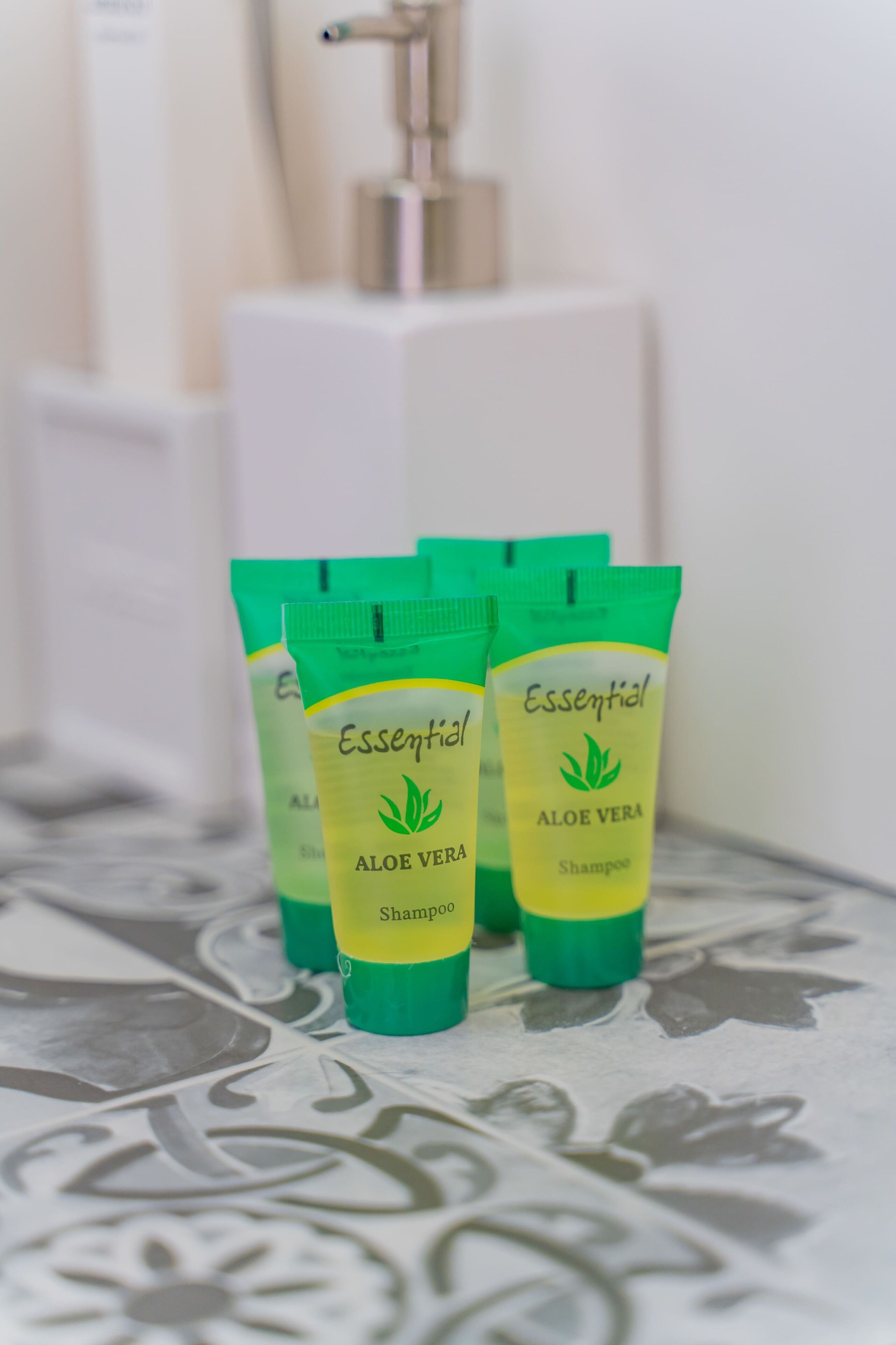 Cuatro tubos verdes y amarillos de Champú de Aloe Vera Essential sobre una superficie estampada.