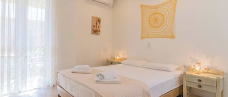 A bedroom with a bed, bedside tables, an air conditioner, a window with curtains, and a wall tapestry.