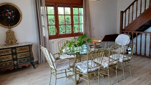 Un comedor con mesa de vidrio, sillas ornamentadas, una araña y vistas amplias a través de grandes ventanales, además de una escalera.