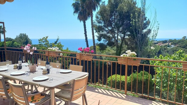 Un área de comedor al aire libre con una mesa preparada para dos, un florero y vista al mar.