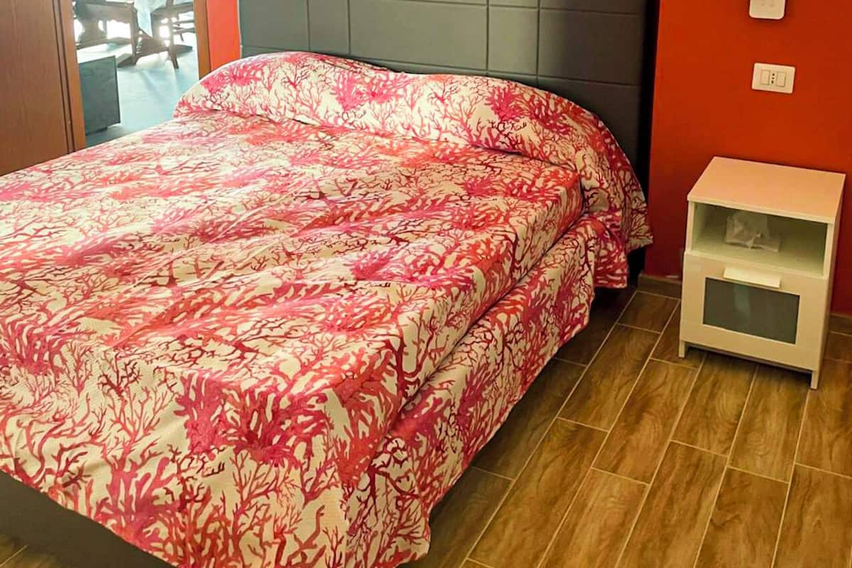 A bedroom with a bed, a nightstand, and a door leading to another room.