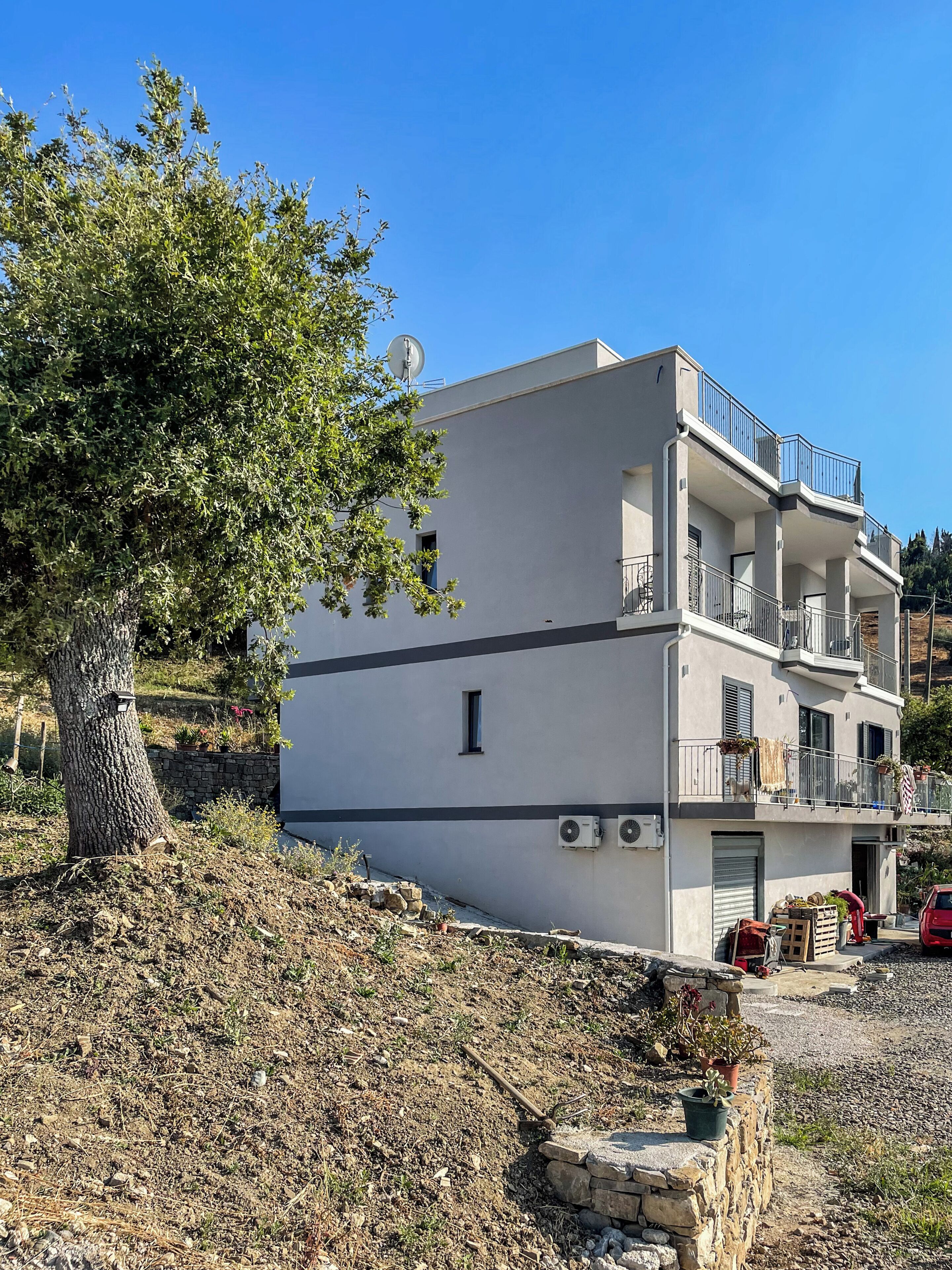 A two-story building with balconies, a satellite dish, and a stone wall.