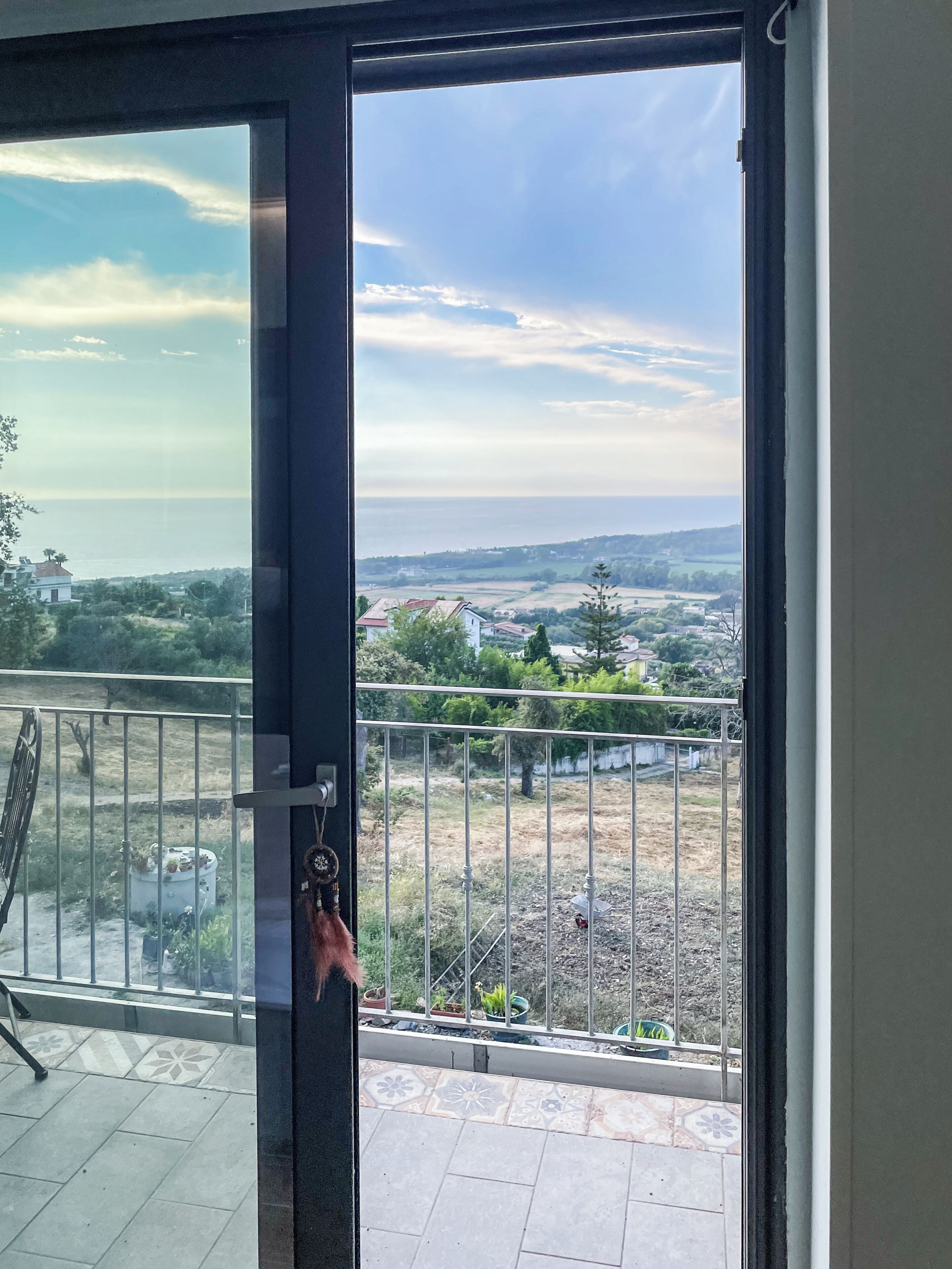 A balcony with a view of a distant landscape, a metal railing, and a door leading to the balcony.