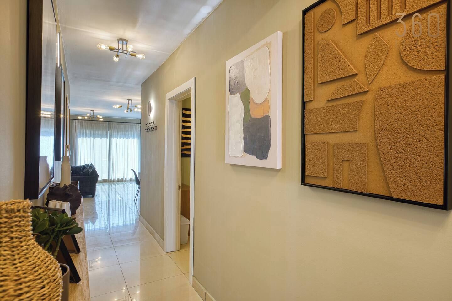 Un pasillo con una decoración moderna, un sofá, una zona de comedor y arte abstracto en la pared.