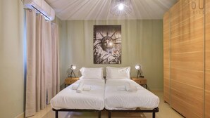 A double bed with white bedding, two bedside lamps, a cityscape artwork on the wall, and a wooden wardrobe.