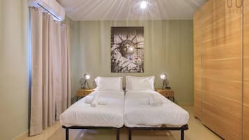 Una cama doble con ropa de cama blanca, dos lámparas de noche, un cuadro de un paisaje urbano en la pared y un armario de madera.