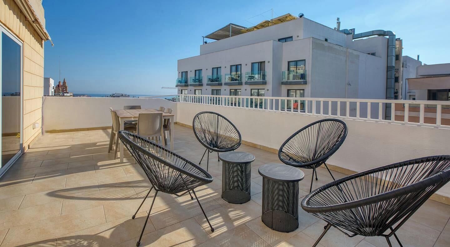 Une terrasse sur le toit avec des sièges extérieurs, une vue sur la mer et un bâtiment moderne en arrière-plan.
