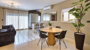 A modern living room with a round dining table, black chairs, a dark sofa, and a large potted plant.