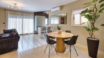 Una sala de estar moderna con una mesa de comedor redonda, sillas negras, un sofá oscuro y una planta grande en maceta.