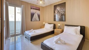 A hotel room with two beds, a large window with curtains, and artwork on the walls.