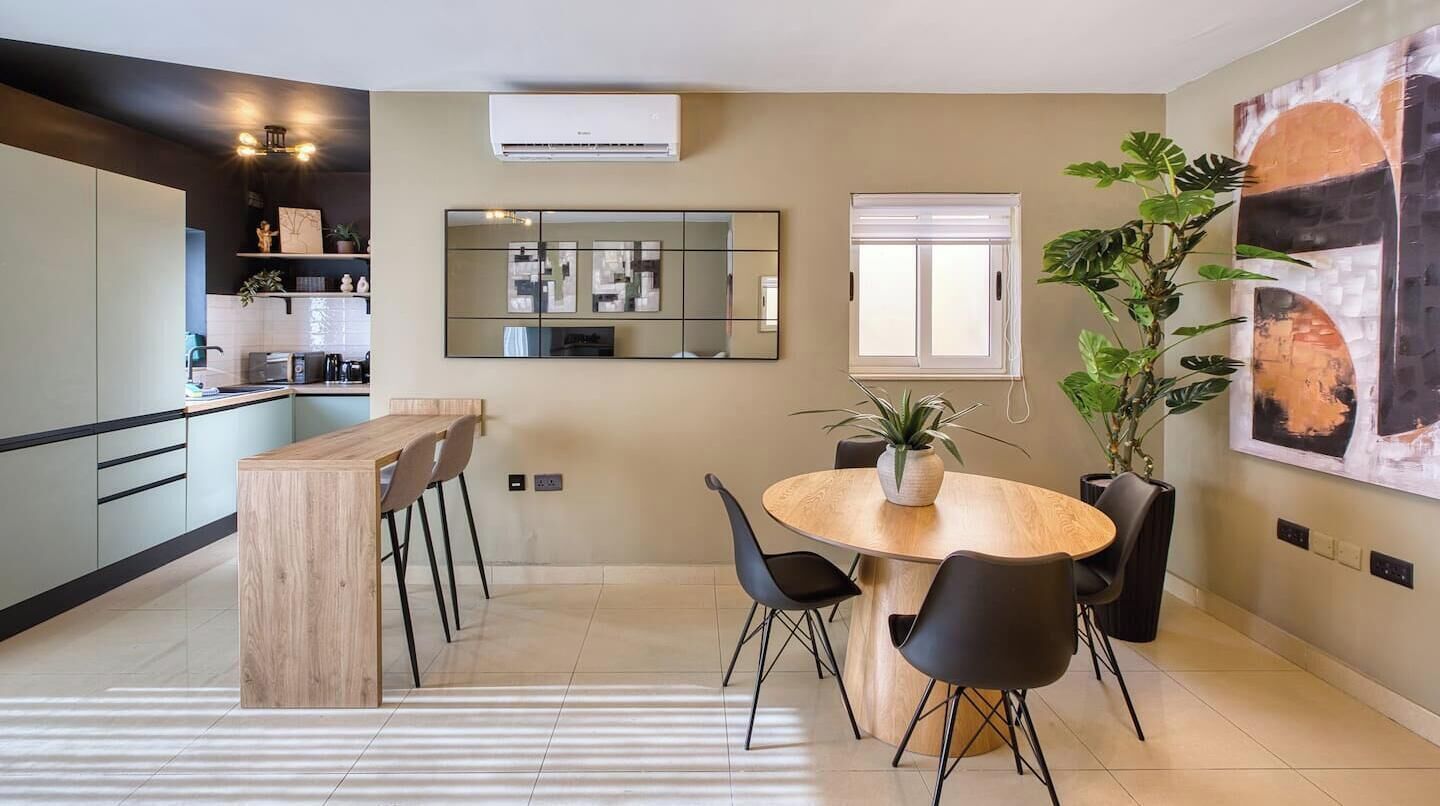 A modern kitchen with a dining area, a large mirror, and a potted plant.