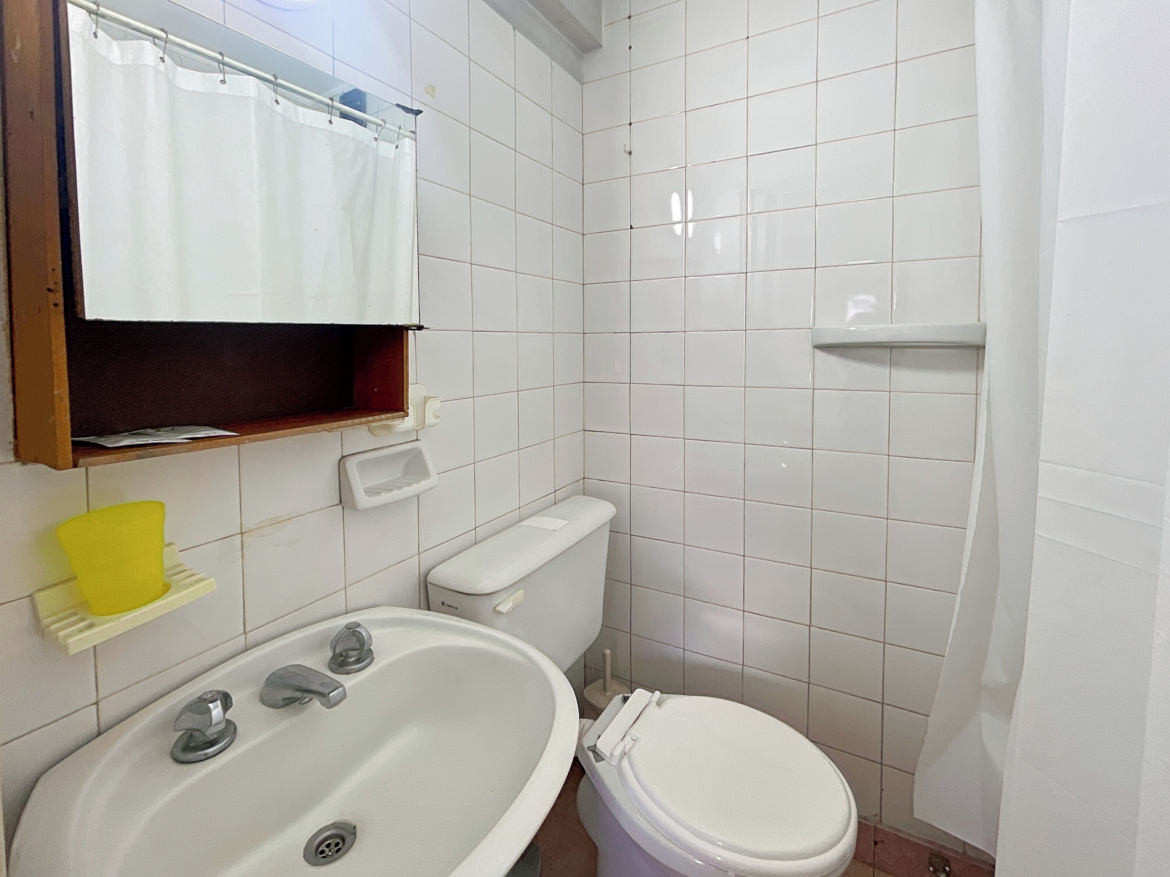 Un bagno con lavandino, wc e tenda per la doccia, tutto in bianco.