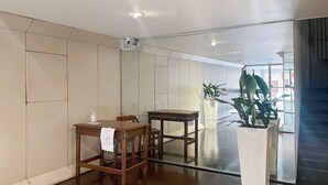 Um quarto amplo com uma mesa e cadeiras de madeira, um vaso branco com uma planta, e uma janela grande que proporciona iluminação natural.
