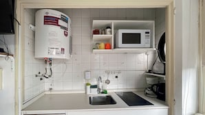 Uma cozinha compacta com aquecedor de água embutido, micro-ondas, pia com torneira e armários.