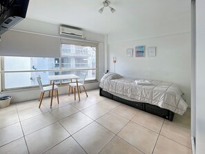 Ein Schlafzimmer mit einem Bett, einem Fenster, einem Tisch mit Stühlen und einer Klimaanlage.