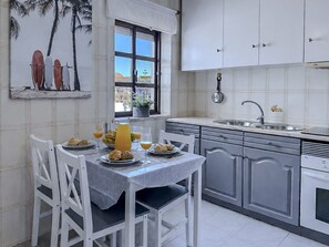Cuina amb armaris blancs, finestra amb vistes i taula de dinar a punt per esmorzar.