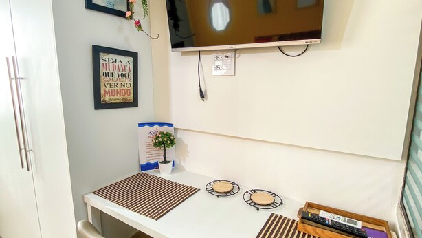 Une petite pièce moderne avec un téléviseur fixé au mur, deux chaises, un bureau avec un plateau et une plante en pot.