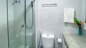 Une salle de bain avec une douche à parois de verre, des toilettes, un porte-serviettes et un lavabo.