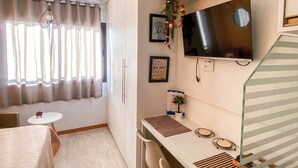 Une chambre moderne équipée d’un téléviseur à écran plat, d’une petite table ronde, de deux chaises, d’un bureau avec un ordinateur portable, d’une plante en pot et d’un objet décoratif rappelant la Tour Eiffel.