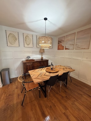 Un comedor con una mesa de madera, sillas negras, una lámpara colgante y obras de arte en las paredes.