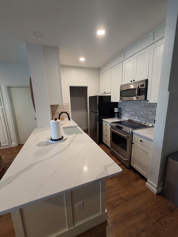 Una cocina moderna con armarios blancos, encimera de mármol, electrodomésticos de acero inoxidable y suelo de madera.