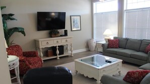 Ein Wohnzimmer mit Fernseher, Sofa, Couchtisch und roten, gemusterten Sesseln.
