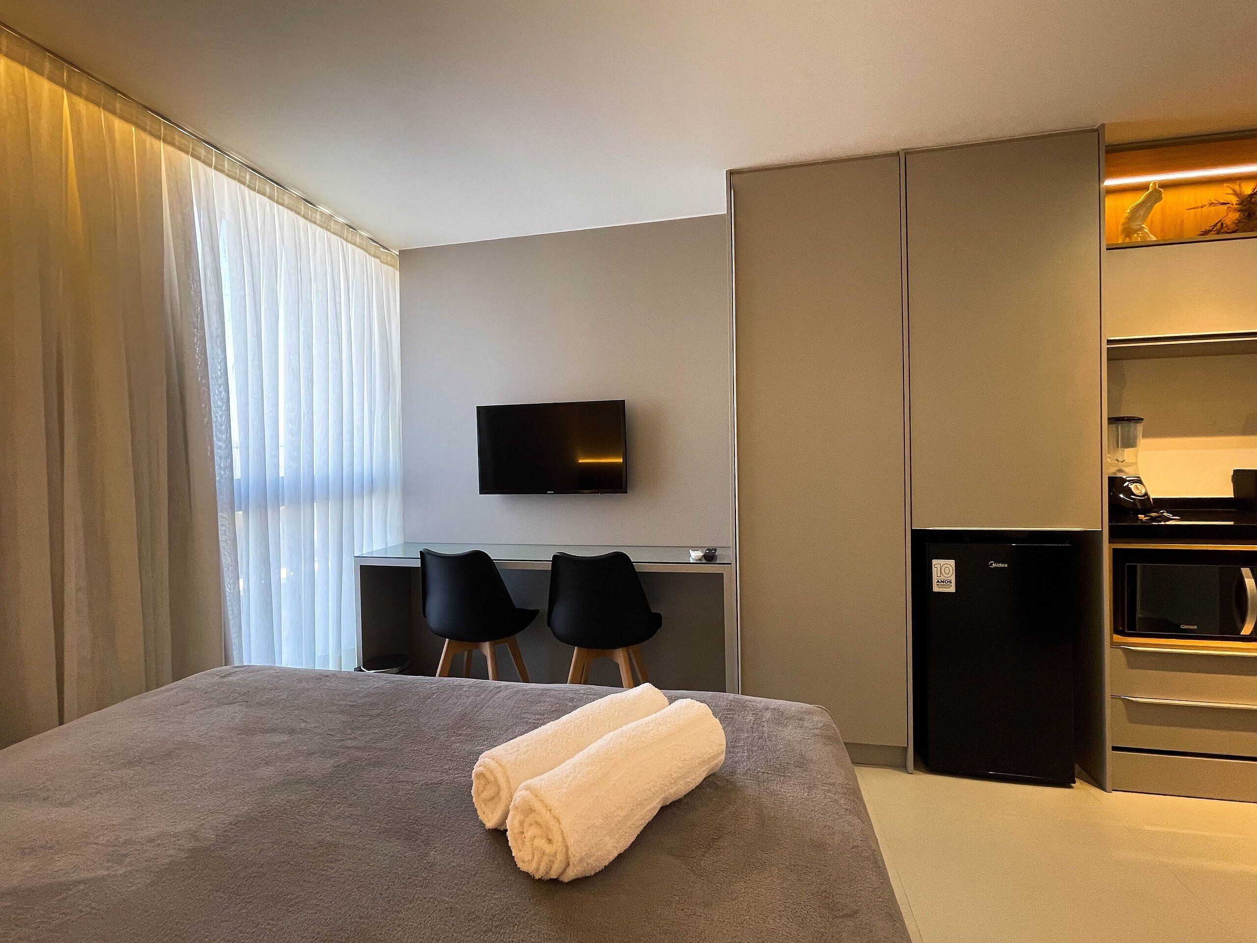 A hotel room with a bed, a desk with two chairs, a television, a refrigerator, and a microwave.