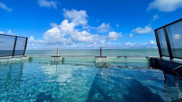 Una piscina infinita con agua cristalina azul y vistas al océano bajo un cielo azul brillante.
