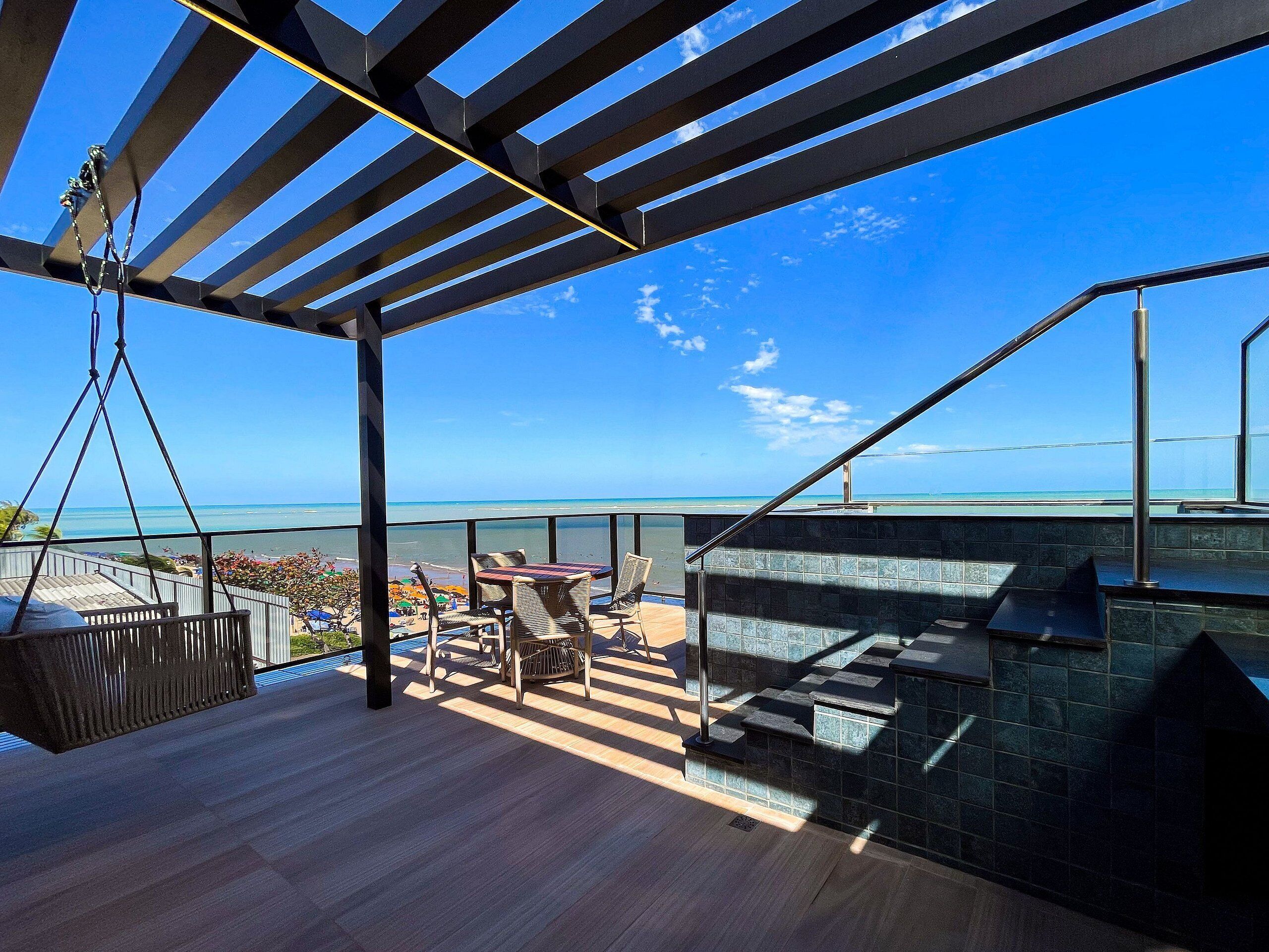 A rooftop terrace with a view of the beach, outdoor seating, and a pool area.