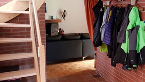 A room with a brick wall, a wooden staircase, a grey sofa, and a clothing rack with various jackets. - Haus Gonzenblick, (Flumserberg Tannenheim), by Interhome (Flumserberg Tannenheim)