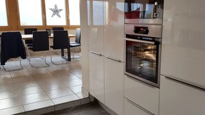 A kitchen with white cabinets, a built-in oven, and a dining area with chairs and a table. - Haus Gonzenblick, (Flumserberg Tannenheim), by Interhome (Flumserberg Tannenheim)