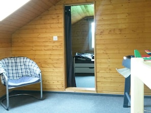 A small, wooden-paneled room with a single bed, a chair, and a desk.