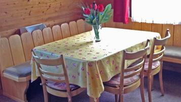 Ein Holztisch mit einer blumigen Tischdecke, umgeben von Holzstühlen mit gepolsterten Sitzen.